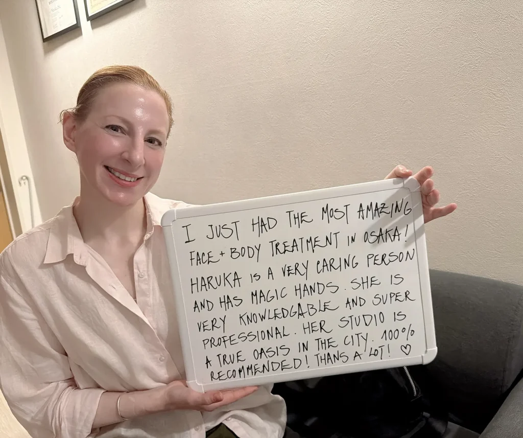 Guest holding a handwritten review praising her face and body treatment with Osaka esthetician Haruka